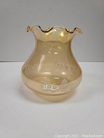 Photo of a yellow-orange glass lampshade with scalloped rim, floral etched designs on smooth glass surface, shown from front on a plain background.
