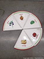 Photo showing five ceramic pizza slice dishes arranged in a circle with one piece missing. Each slice features a different hand-painted vegetable or cheese design with red and green trim.
