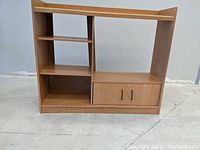 Front view of the light brown TV cabinet with shelving on left side, middle shelves, and closed storage with doors on right side.