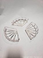Three clear quarter-circle glass dishes arranged separately on white background, showing fan pattern and scalloped edges