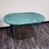 Green plastic outdoor oval table with visible wear on surface and legs, photographed from an angle to show top and legs.