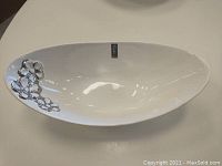Full view of elongated white ceramic serving bowl with silver flower detail at one end.