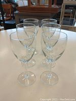 Front angled view of six clear wine glasses arranged on a white round table.