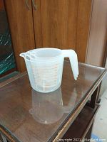 Single 2-cup translucent plastic measuring cup with orange measurement markings and handle sitting on wood cabinet top.