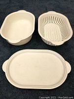 Three-piece set including casserole dish, strainer insert, and lid, arranged separately on dark cloth.