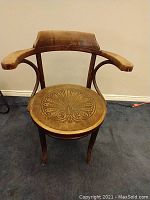 Front angle of the wooden chair showing curved arms and carved round seat design.