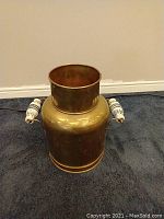 Full view of the brass planter showing its cylindrical shape and porcelain handles on both sides.