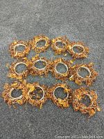 Full view of all 12 silver napkin rings decorated with numerous amber colored beads and stones, arranged on a grey surface.