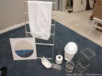 Photo showing entire bathroom set including white metal towel rack with towel, small white garbage bin, toilet roll holder with paper, shower curtain rings, shower caddy, and white ceramic bathtub soap dish.