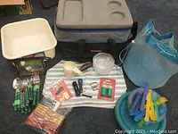 Photo showing the entire camping kit collection including cooler bag, mesh bucket, plastic wash basin, green handle cutlery, plastic bowls and plates, striped placemats, small flashlights, multi-tool, travel bottles, toothpicks, clothespins, and a sealing clip.
