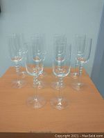 Ten clear champagne flutes with beaded stems arranged on a wooden surface.