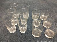 Set of six tall and six short clear drinking glasses arranged on carpet. The tall glasses are approximately 6.5 inches high, the shorter glasses approximately 4 inches high.