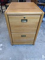 Front view of wooden filing cabinet showing two drawers, label holders, and key lock on top drawer. Light scratches and scuffs visible on wood surface.