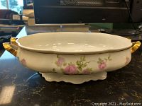 Side angle view of oval Fraureuth porcelain serving bowl with pink rose floral pattern and gold handles on black surface.