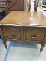 Square wooden end table with two paneled doors and brass hardware, detailed turned legs visible.
