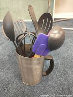 Kitchen utensils placed within metal milk bag holder showing handle, spatulas, ladle, and turners