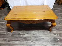 Front view of rectangular wooden coffee table showing the Queen Anne cabriole legs and carved apron detail.