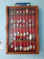 Wooden display case showing approx 30 collector spoons arranged in three rows