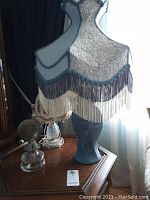 Vintage blue fabric table lamp with lace overlay and blue fringe trim, ceramic base.