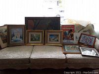Wide shot of couch displaying multiple framed art prints and posters including the metal Gone with the Wind movie poster and framed San Francisco cheerleaders photo.