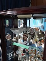 Showcase with porcelain miniature china items including cake platters, decorative plates, small cups, and figurines inside a glass cabinet.