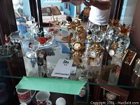 Assorted crystal figurines including pineapples, clocks and decorative pieces displayed on glass shelf