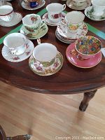 Nine vintage porcelain teacups and saucers displayed on a wooden table showing various floral patterns and colors.