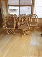 Five natural finish rattan chairs including two swivel and three fixed chairs grouped in a room