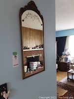 Full view of the vertical vintage wall mirror hanging on a wall, showing the carved metal frame and the reflective surface.