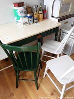 View of vintage kitchen table showing cream enamel tabletop, green wooden base, and items placed on top including tins and bottles.