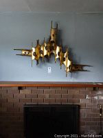 Full view of metal wall art hanging above fireplace, showing overall design and dimensions.