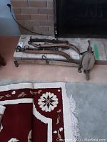 Full view of the antique horse harness placed on a carpeted floor in front of a fireplace showing two long curved wooden wooden harness parts and fastened metal hardware.