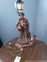 Lamp on wooden end table showing fisherman figurine base, lamp post, and lamp cord