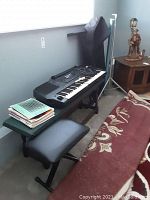 Wide view of keyboard on stand with bench beside it, music sheets on bench, and carrying bag upright in corner.