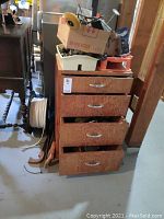 Wooden storage cabinet with four drawers partially open, boxes with tools on top.