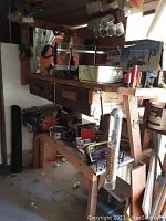 Wide view of wooden workbench with miter saw, paint can, bird feeder tube with birdseed, and various tools on top and shelves below.