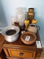 Photo of all vases, bowls, and candlesticks on a wooden surface showing variety of materials and styles.