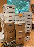 Stack of twenty banker boxes, some white and some brown, filled with books for sale.