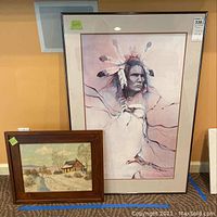 Both signed art pieces displayed: Native American large print in glass frame and smaller rural house painting in wooden frame.