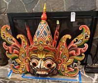 Front view of carved wooden Barong mask against stone backdrop