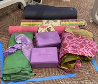 Photo showing Manduka yoga mat, three carrying cases, two yoga towels with Gaiam logo, two purple Gaiam yoga blocks, yoga strap, and Mysore rugs