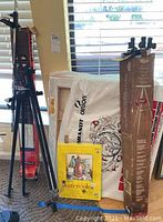 Art supplies including a large white bag branded 'Brandt Carson', a watercolor paper pad showing a watercolor painting of bottles and glass, and rolled canvases behind these items.