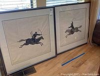 Two framed ink drawings of Japanese archers on horses side by side, showing entire framed pieces leaning against a wall.