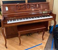 Front view of Baldwin Acrosonic upright piano with carved wooden music rack and matching bench.