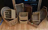 Photo showing a variety of 13 woven baskets of varying shapes and sizes arranged on wooden floor, including some with compartments, handles, and open design.
