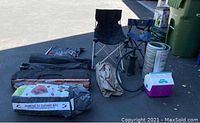 Overview of camping equipment including tent bag, two collapsible chairs in different colors, cooler, air mattress with pump, thermal mat, and jumbo camp shower bag.