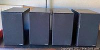 Four black rectangular Camber 5 bookshelf speakers placed side by side, showing front and top view. Visible scratches on cabinet surfaces.