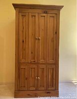 Front view of closed knotty pine armoire showing four paneled doors with wooden knobs.