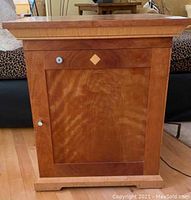 Front view of the wooden humidor cabinet showing door, drawer, diamond inlay, and metal knobs.