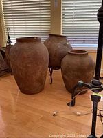 Three large decorative olive pots on wood floor near window blinds